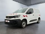 La camionnette blanche est garée à l'intérieur d'un bâtiment ; elle porte une bande rouge sur le côté.