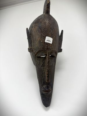 a wooden mask hanging on the wall with a tag on it