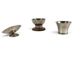 two silver cups and a silver spoon on a white surface