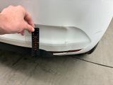 someone is measuring the front bumper of a white car with a ruler