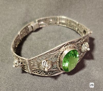 silver bracelet with a green stone in the middle of it on a gray surface