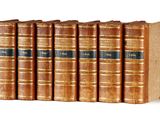six old books are lined up in a row on a white surface
