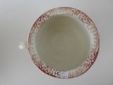 a red and white bowl with a handle on a white table