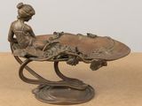 a bronze statue of a woman sitting on a leaf shaped table