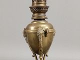 une lampe ancienne en laiton surmontée d'une tête de lion