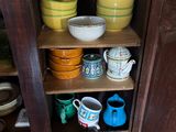 many bowls and cups sitting on a shelf in a cabinet
