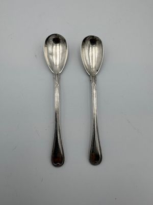 une paire de cuillères en argent posées sur une surface blanche avec un point noir