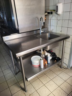 a stainless steel table with a sink and a refrigerator in the background