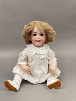 une image représentant une poupée en porcelaine assise par terre, vêtue d'une robe blanche et de chaussures marron