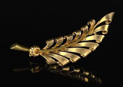 a close up of a gold leaf brooch on a black surface