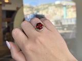 woman ' s hand holding a ring with a red stone in it