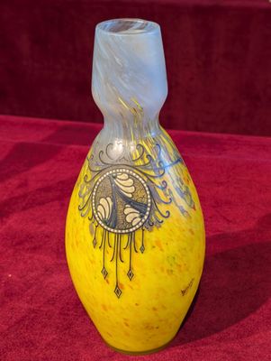 un vase jaune orné d'un motif, posé sur un tissu rouge