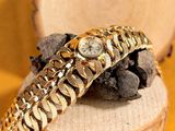 a gold bracelet with a watch on it on top of a piece of wood
