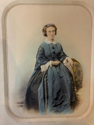 une vieille photo d'une femme en robe bleue, assise sur une chaise
