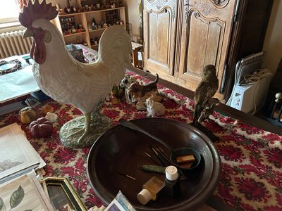 une statue de coq posée sur une table, à côté d'un bol de vin