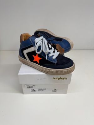 des baskets bleues et blanches avec une étoile orange sur le côté, présentées dans une boîte