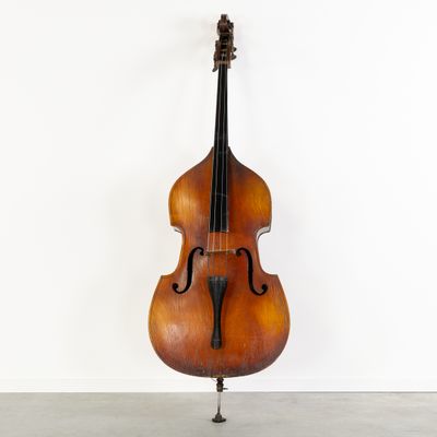 un vieux violoncelle posé sur un pupitre, adossé à un mur blanc