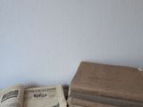 Plusieurs vieux livres sont empilés sur une table, avec un mur blanc en arrière-plan.