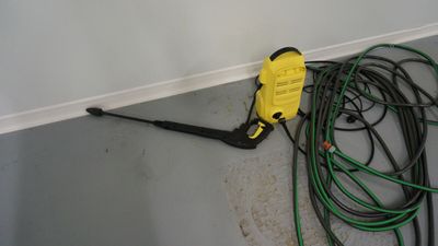 a yellow pressurer sitting on the floor next to some green hoses