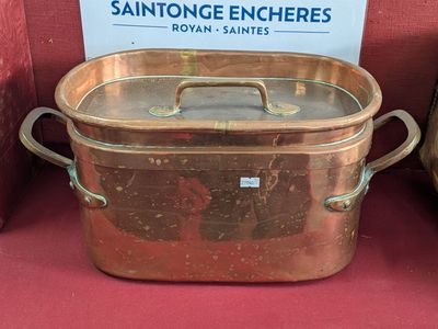 une grande casserole en cuivre posée sur une table rouge