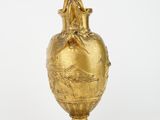 an antique gold vase with a bird on it on a white background