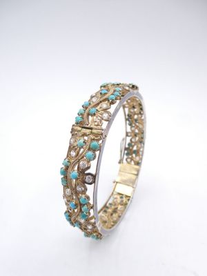 a close up of a gold and turquoise bracelet on a white background