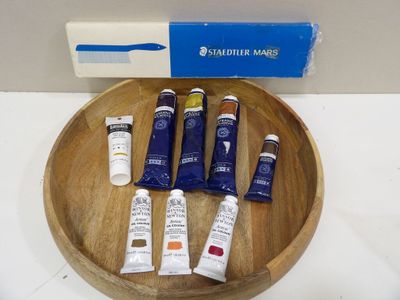 a wooden bowl with various tubes of paint on it