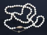un collier de perles blanches avec un fermoir en or sur fond noir