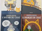 trois livres posés sur une table blanche, avec un chat et un autre chat assis sur une chaise