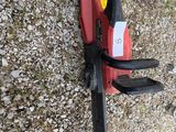 a red and black chainsaw on the ground next to a cat