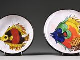 two plates with fish painted on them sitting on a table