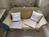 a wicker couch with two pillows on it in the corner of a room