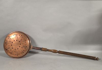 an antique copper strainer with a wooden handle on a white background