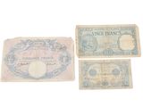 Trois anciens billets de banque français sont posés sur une surface blanche