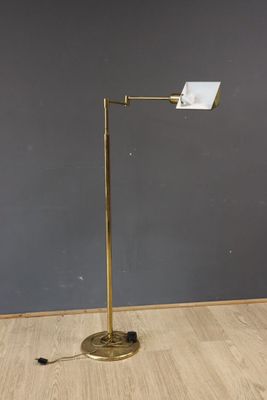 Le lampadaire est posé sur un parquet, devant un mur gris.