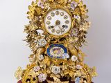 une horloge dorée posée sur un socle rouge orné de fleurs
