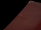 an old red book with gold trim sitting on a black surface