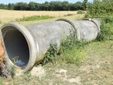 a giraffe standing next to a large pipe in a field