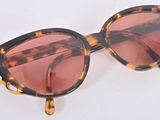 lunettes de soleil à monture écaille avec des verres teintés en rose sur fond blanc