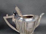 a silver teapot with a bird on the handle