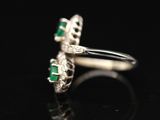 a close up of a diamond and emerald ring on a black surface