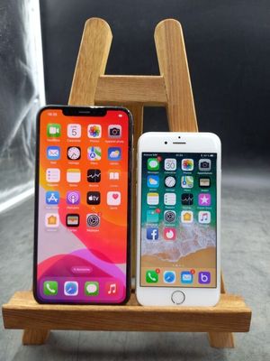 deux iPhones posés sur un support en bois à côté d'un verre d'eau