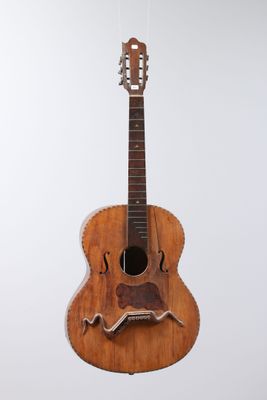 an old wooden guitar hanging from a string on a white wall