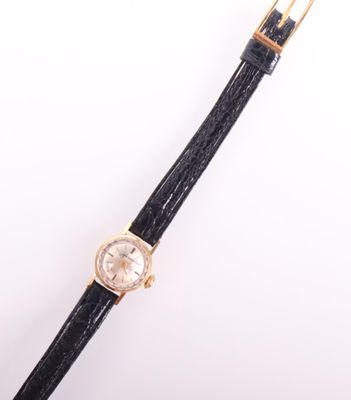 un gros plan d'une montre avec un bracelet noir posée sur une surface blanche