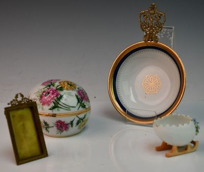 une assiette blanche ornée d'une couronne dorée, à côté d'un œuf et d'un cadre photo
