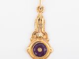 a close up of a gold pendant with a purple stone