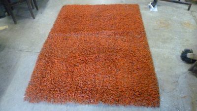 un tapis orange posé au sol dans une pièce où se trouvent des chaises et une table