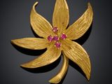 un gros plan sur une broche en forme de fleur en or sertie de pierres roses