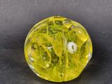 translucent yellow glass bead with green and white designs on a black surface