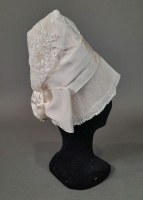 chapeau blanc orné d'un nœud et d'une bordure en dentelle, posé sur une tête de mannequin